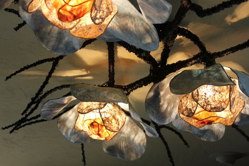 A cluster of shell-shaped paper lanterns glowing along a black branch armature.