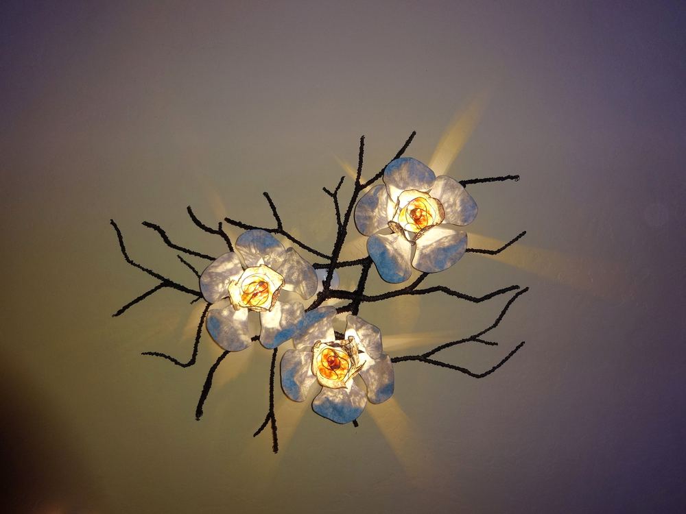 A wall-mounted branch sculpture carrying several illuminated blossom-shaped shades.