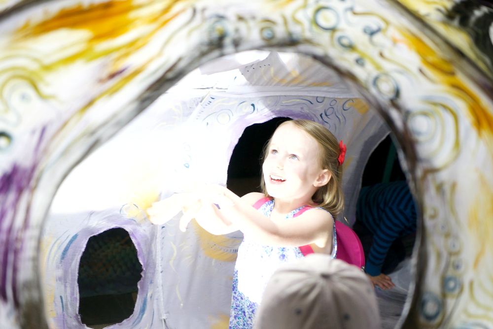 A delighted child standing inside the mouth of a large white painted sculpture, reaching out.