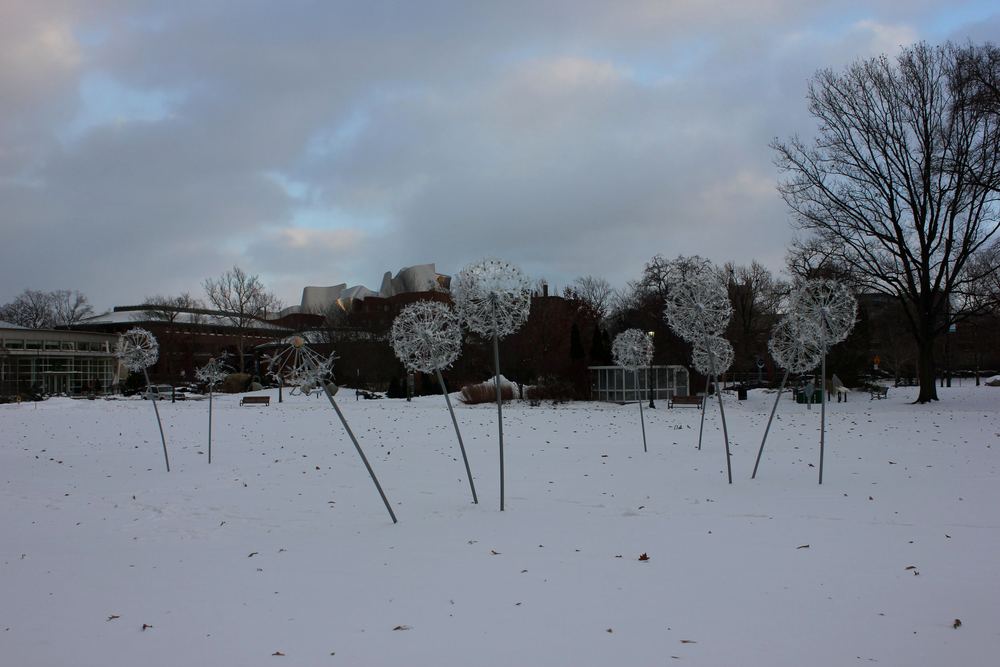 Giant dandelion sculptures standing in a snow-covered field under a grey winter sky.