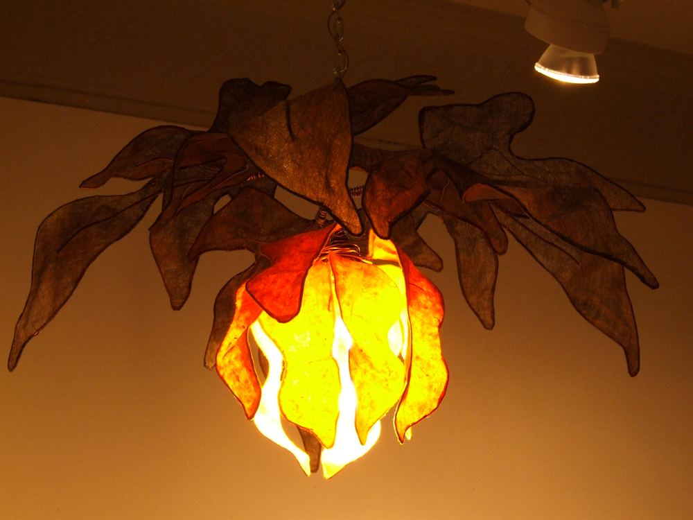 A paper lantern shaped like a flame glowing orange inside a canopy of translucent paper leaves.