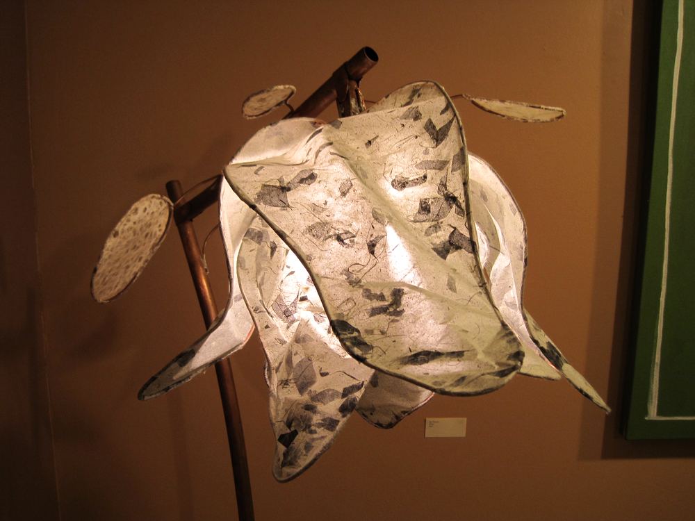 A sculpture of a pale moth or leaf form mounted on rods against a warm gallery wall.
