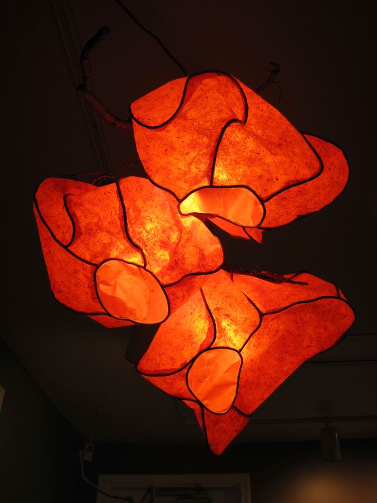 Glowing orange paper forms suspended from a ceiling, lit from inside.