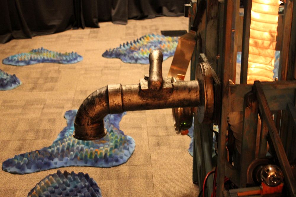 A close detail of a copper pipe fixture with small painted fish forms swimming along the wall beside it.