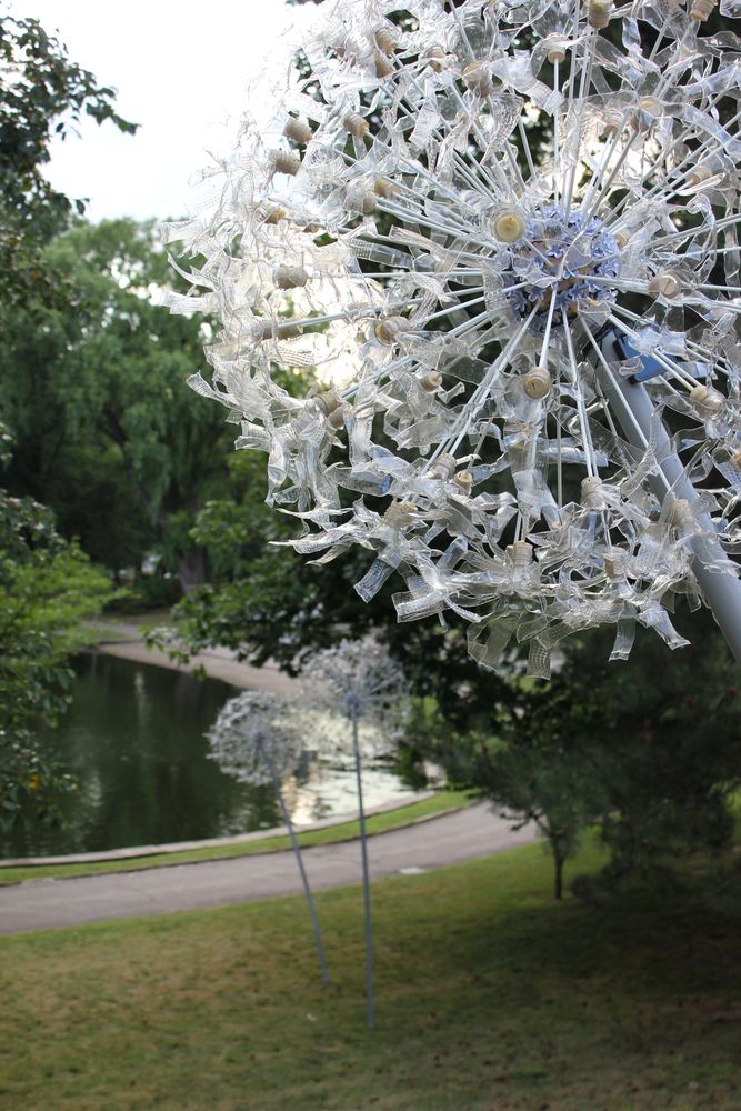A white dandelion seedhead sculpture standing among trees in a park.